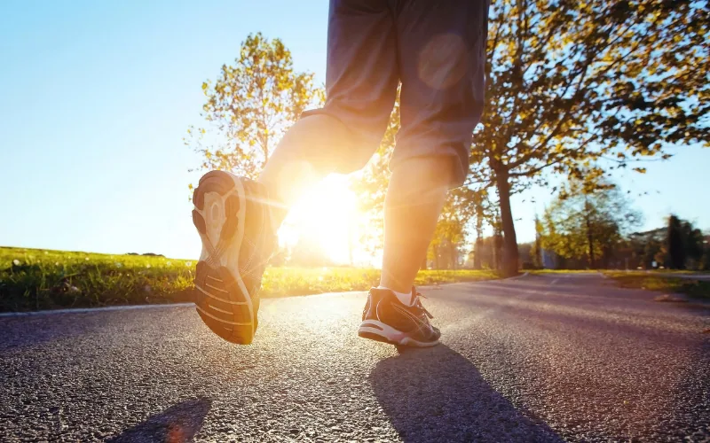 Jambes d'un coureur sur une route asphaltée à contre-jour du soleil