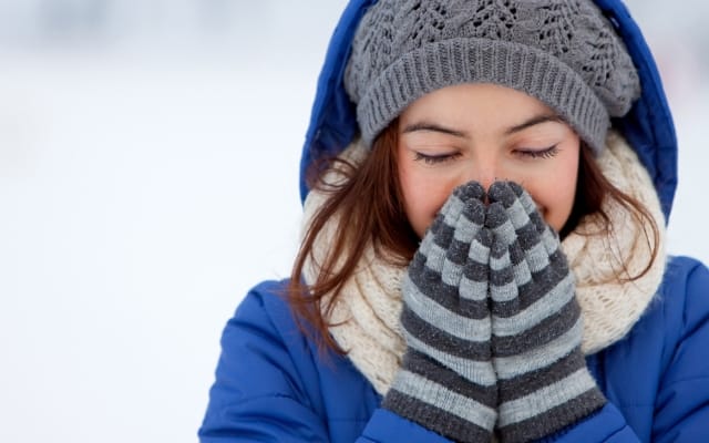 Femme emmitouflée en hiver soufflant sur ses mains gantées