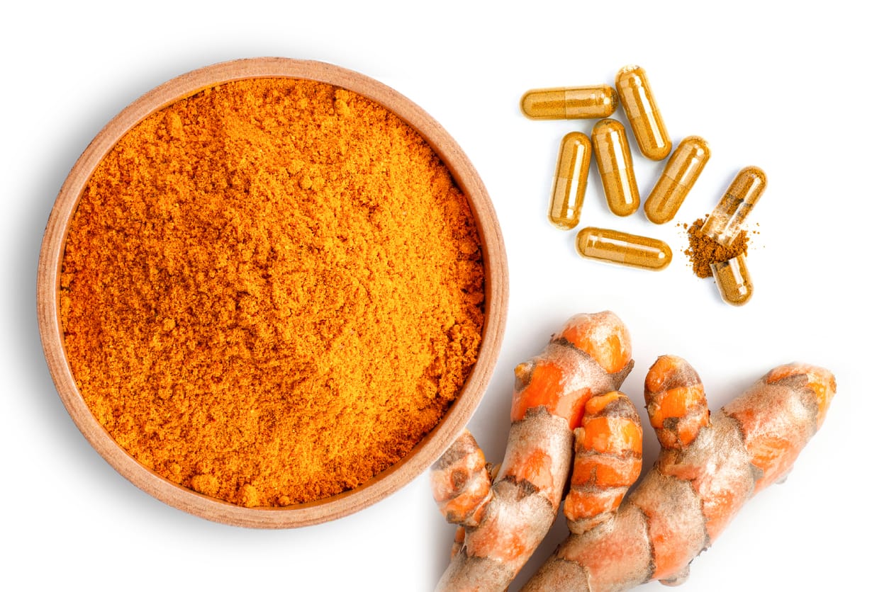 Poudre de curcuma dans un bol en bois, gélules et racines de curcuma fraîches