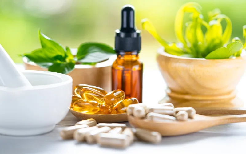Gélules, capsules molles et flacon compte-gouttes ambré entre des plantes fraîches