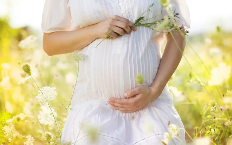 Femme enceinte en robe blanche dans un pré fleuri