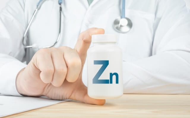 Médecin tenant un flacon blanc portant le symbole du zinc Zn