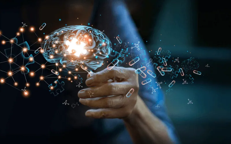 Main tenant un cerveau lumineux entouré de connexions et de gélules